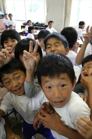 Children in a bright classroom, some making peace signs, others smiling broadly.