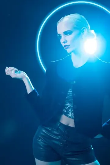MADY in black attire, illuminated by blue neon halo against dark backdrop.