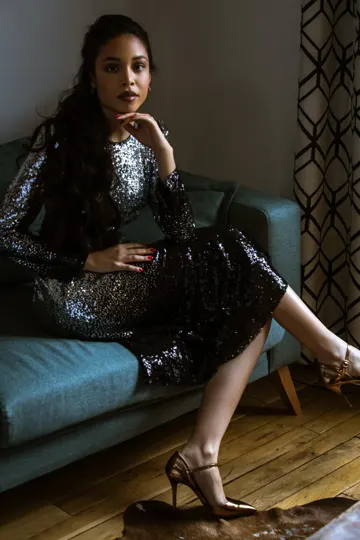 A woman in a sequined dress lounges on a blue sofa, lit softly.