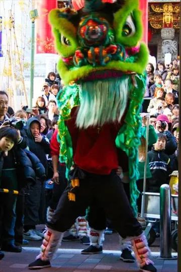 A vibrant green dragon costume performer dances before a crowd under bright daylight.