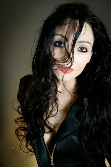 Subject with long, dark, wavy hair in a black leather jacket, soft studio lighting.