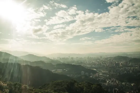 Golden hour light bathes a cityscape nestled among rolling green hills.