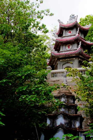 Ancient stone pagoda, red-tiled roof, nestled in dense green foliage.