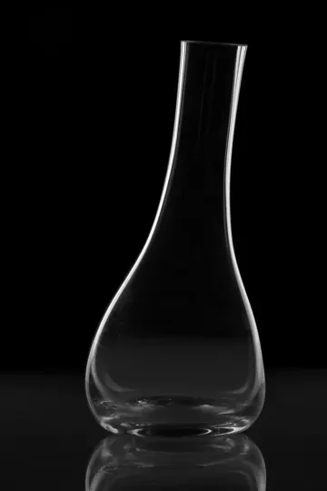 A clear glass vase stands against a pitch-black background, illuminated by soft, directional light.
