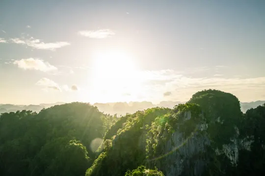 Golden light bathes verdant limestone peaks under a clear sky.