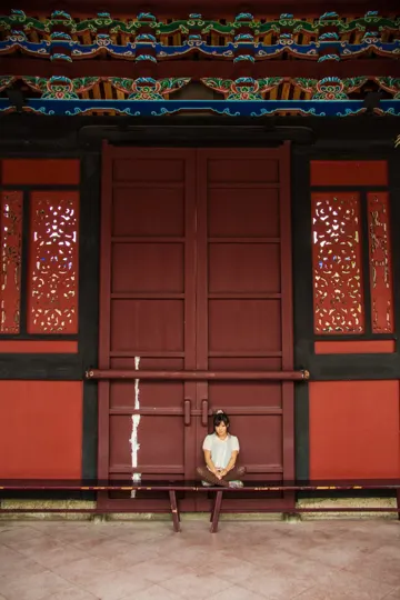 A contemplative figure sits before a vibrant, traditional wooden gate.