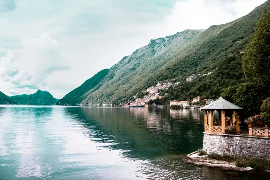 Lake waters reflect green mountains under a soft, overcast sky.