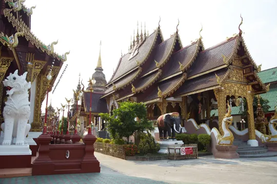 Golden temple roofs and white stone guardian statues under soft daylight.