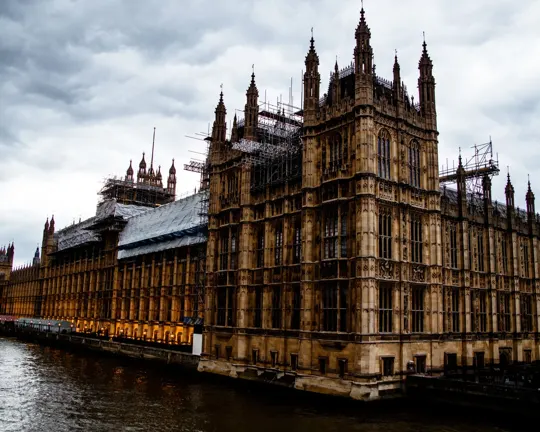 Gothic architecture along the Thames, overcast sky, warm interior lighting.
