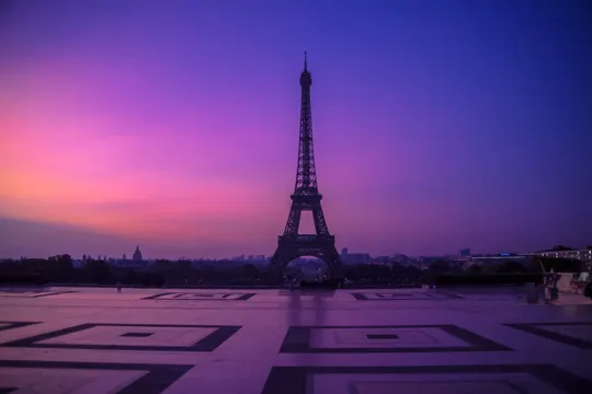 Eiffel Tower silhouetted against a gradient sky at dusk, with geometric plaza foreground.
