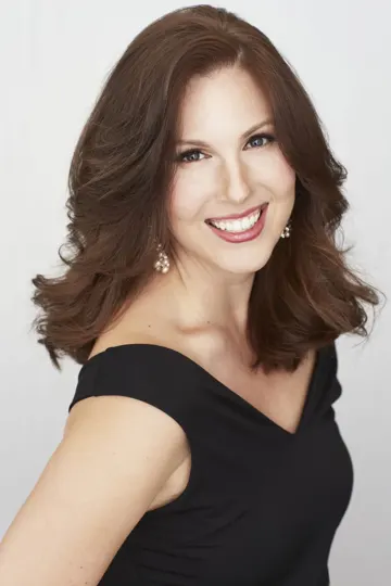 A woman with shoulder-length brown hair wears a black off-the-shoulder top against a plain white background.