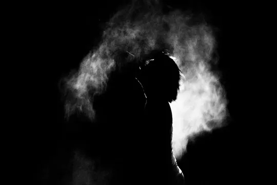 Silhouette of a person enveloped in billowing smoke against a dark background.