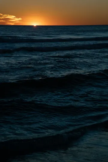 Sunset casts golden light over rolling ocean waves at dusk.