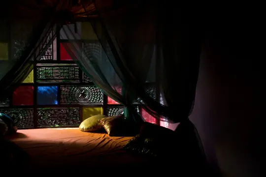 A dimly lit bedroom with a bed under a colorful stained-glass window.