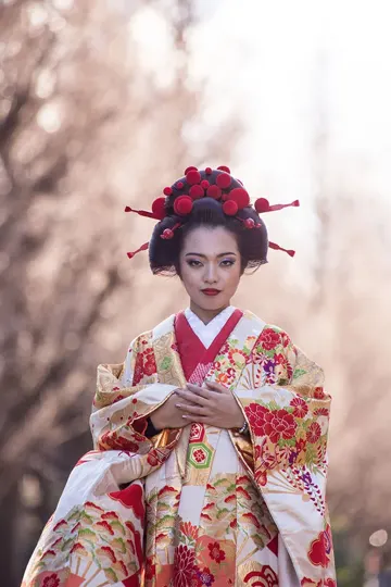 A woman in a traditional Japanese kimono stands amidst softly blurred cherry blossoms, bathed in warm, diffused light.