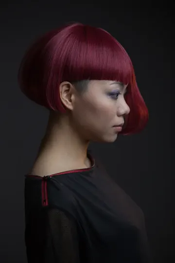A woman with a sleek, vibrant red bob haircut, profile against a dark background.