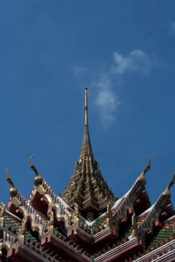 Golden spire pierces clear blue sky, intricate temple roof details catch sunlight.