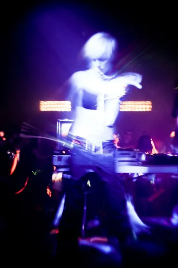 A blurred figure in motion, illuminated by stage lights in a dimly lit venue.