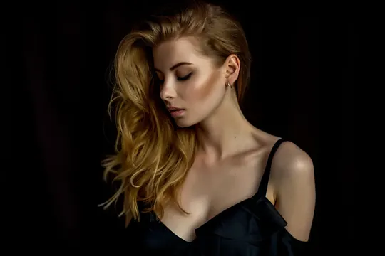 Golden curls cascade against a dark backdrop, illuminated by soft, directional light.