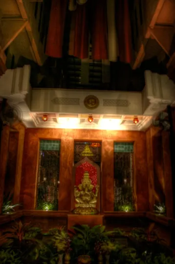 Golden deity statue illuminated by warm light, flanked by stained glass windows and red curtains.