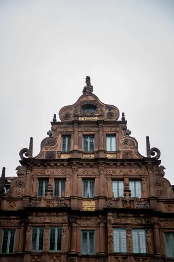 Baroque facade with ornate stonework and Latin inscriptions under overcast sky.