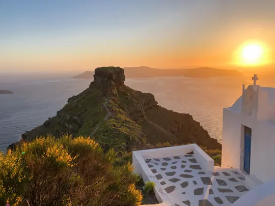 Sunset over the Aegean Sea, with a white-washed church and rugged cliff.