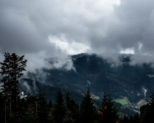 Misty clouds drift over a forested mountain range under a brooding sky.