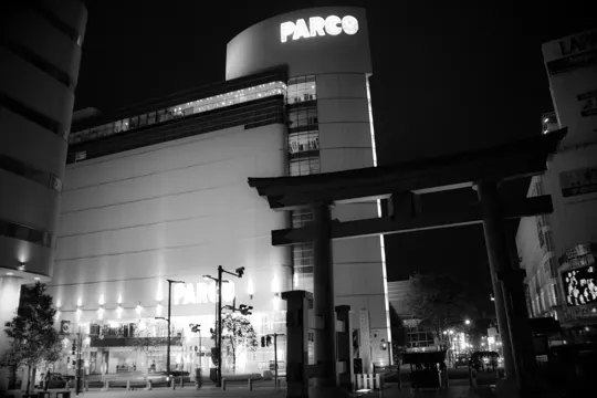 PARCO building illuminated at night, with traditional torii gate in foreground.