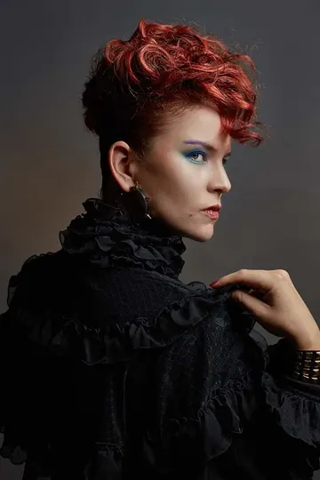 Curly red hair, black ruffled garment, dark studio with soft side lighting.
