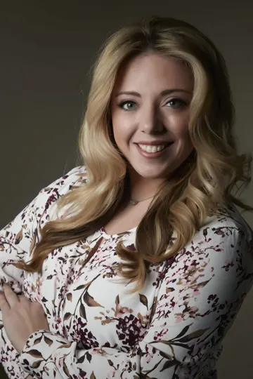 Blonde woman in floral blouse, soft studio lighting, neutral background.