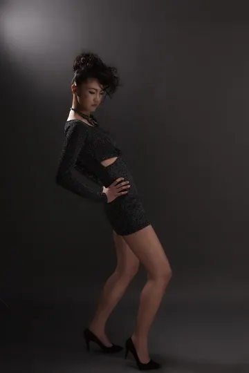 Subject in black textured mini-dress, dramatic lighting, dark studio backdrop.