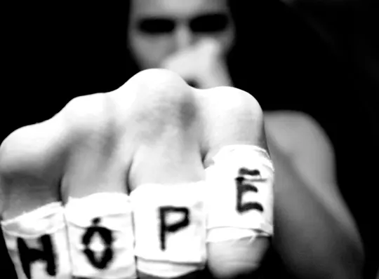 A clenched fist wrapped in bandages spells "HOPE," set against a dark, indistinct background.
