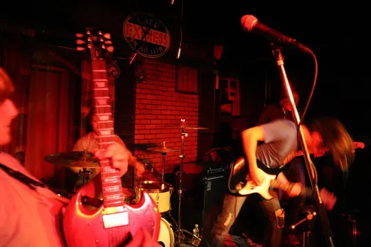 Dimly lit brick-walled venue with musicians performing under red stage lights.