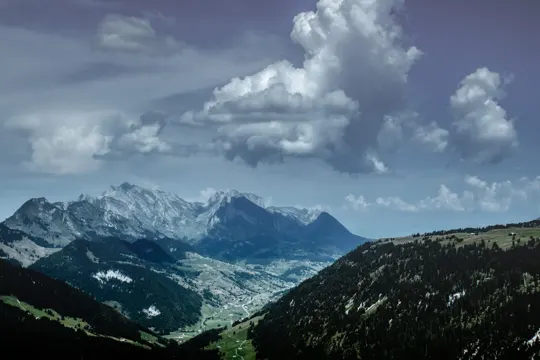 Mountain peaks rise under a dramatic sky, with valleys and forests below.
