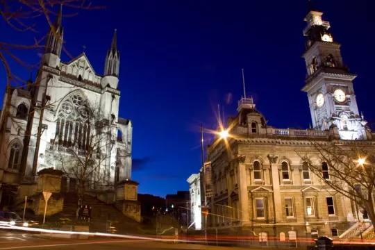 Gothic cathedral and clock tower illuminate a twilight cityscape with streetlights.