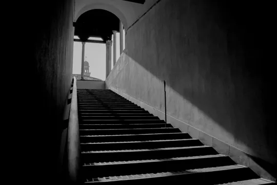 Sunlight illuminates a concrete staircase leading to an arched passageway.
