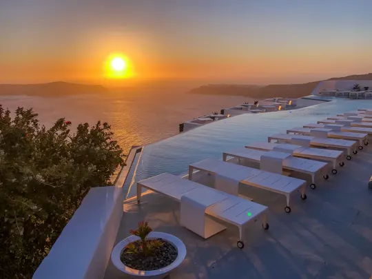 Sunset over the Aegean Sea, infinity pool reflecting golden light.