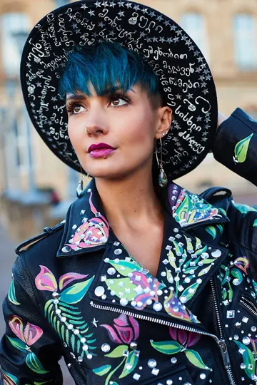 Subject in vibrant floral jacket and script-adorned hat, urban backdrop, soft natural light.
