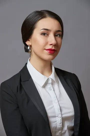 Subject with dark hair, white collared shirt, black blazer, gray background, soft lighting.