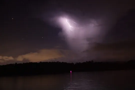 A single pink light glows on a calm lake under a dramatic lightning strike.