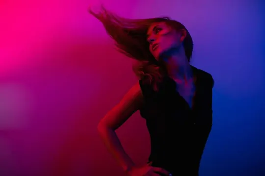 Subject in motion, hair caught mid-swing, bathed in red and blue light.