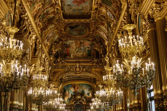 Ornate gold ceiling and chandeliers illuminate a grand, historic theater interior.