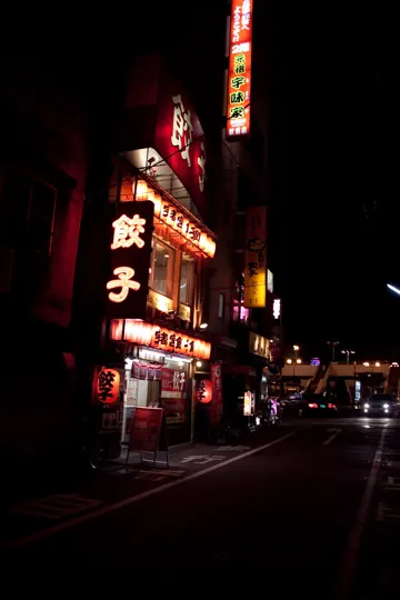 Illuminated Japanese restaurant signs glow against a dark urban street at night.