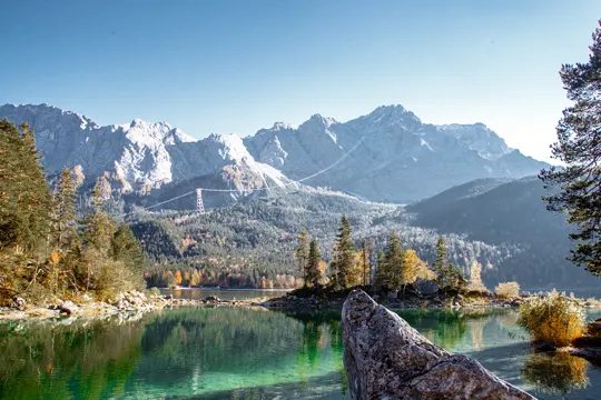 Alpine peaks reflect in a clear lake, framed by autumn trees and a crisp blue sky.