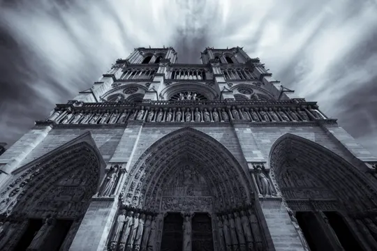 Gothic cathedral facade rises under dramatic, swirling storm clouds.