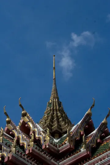 A golden spire rises against a clear blue sky, framed by ornate, colorful temple roofs.