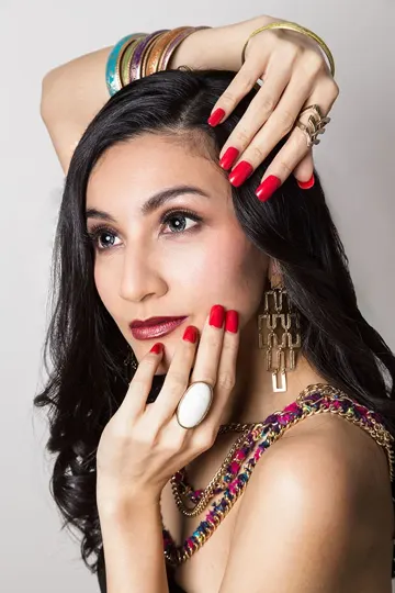 Subject with long dark hair, vibrant red nails, and gold jewelry in soft, neutral setting.