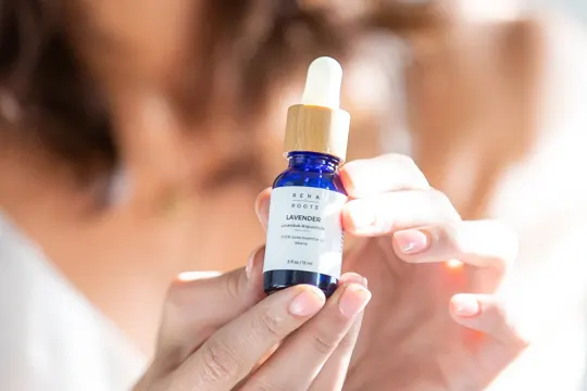 A hand holds a blue glass bottle of lavender essential oil, softly lit.